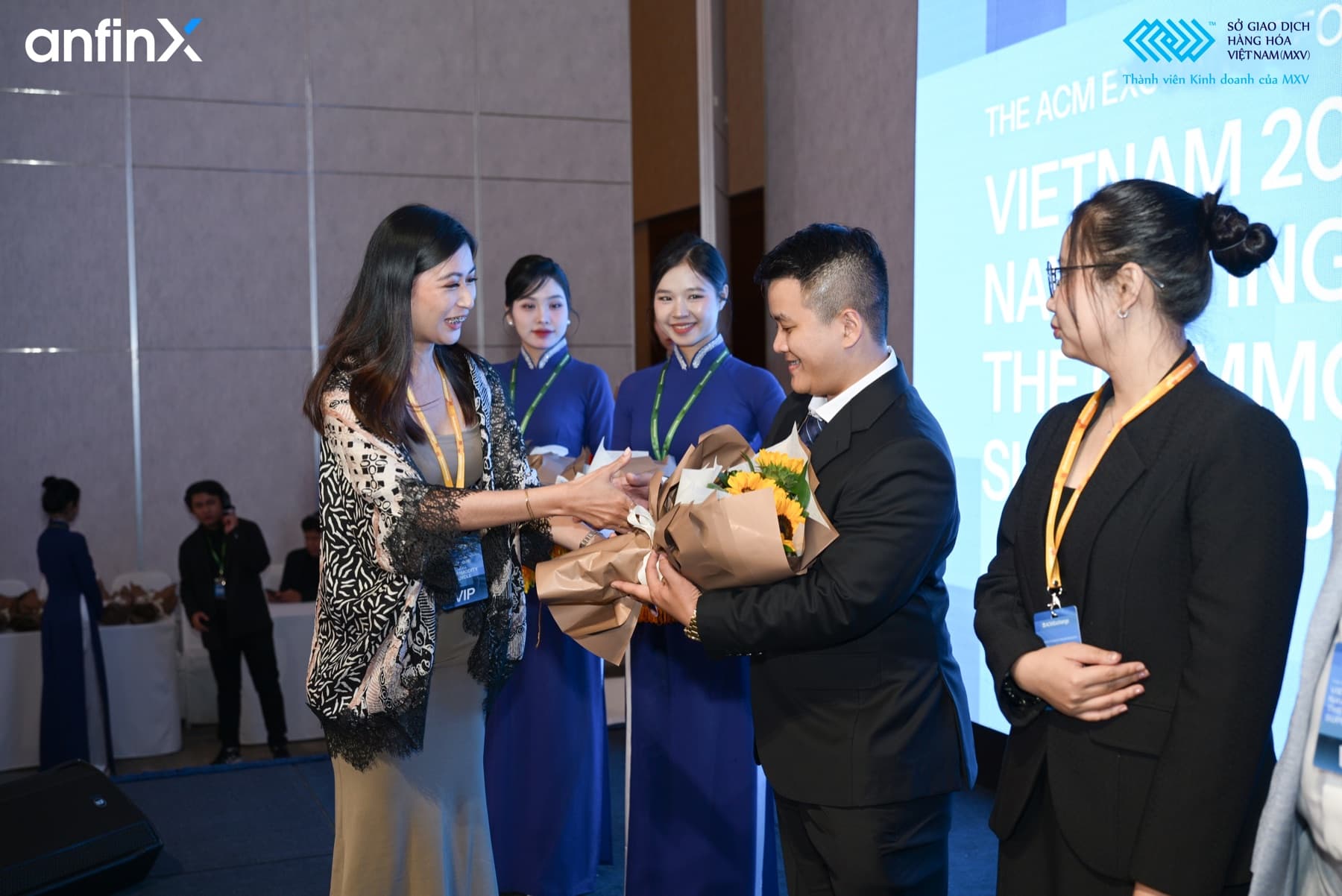 Huỳnh Thanh Tân in a dark suit, holding a bouquet at an event.